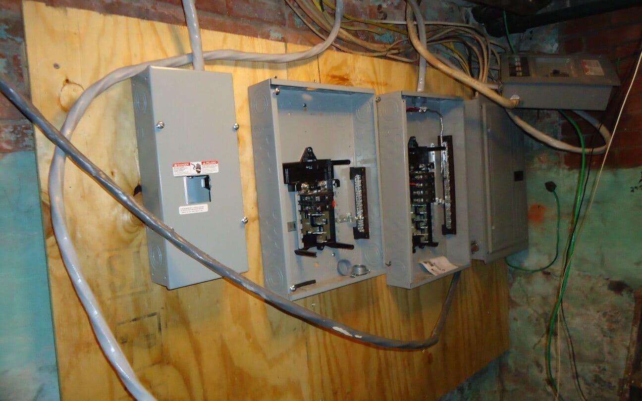 Open residential breaker panels and a service disconnect being wired in a basement