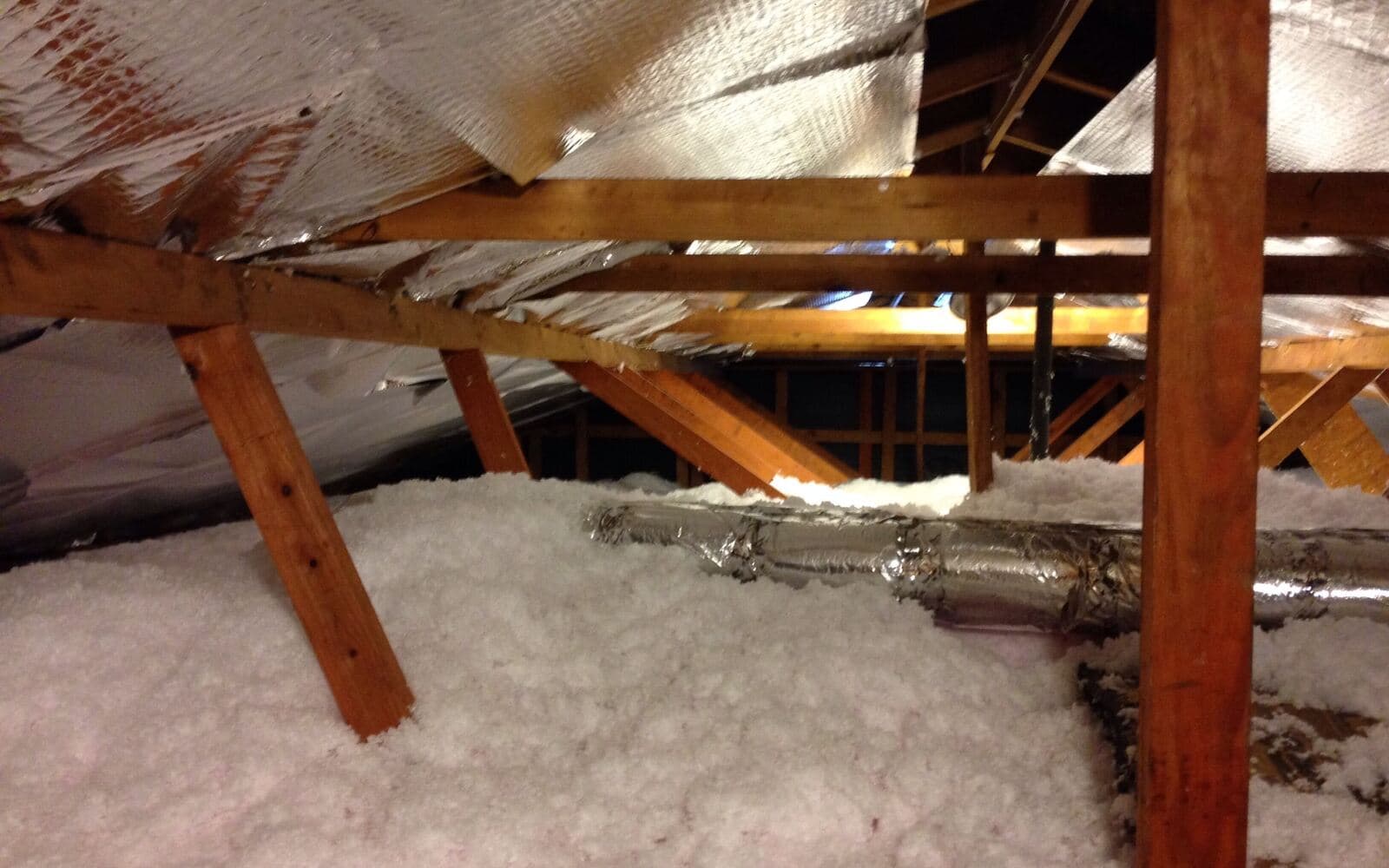 Blown-in attic insulation between rafters with a foil radiant barrier and insulated ducts