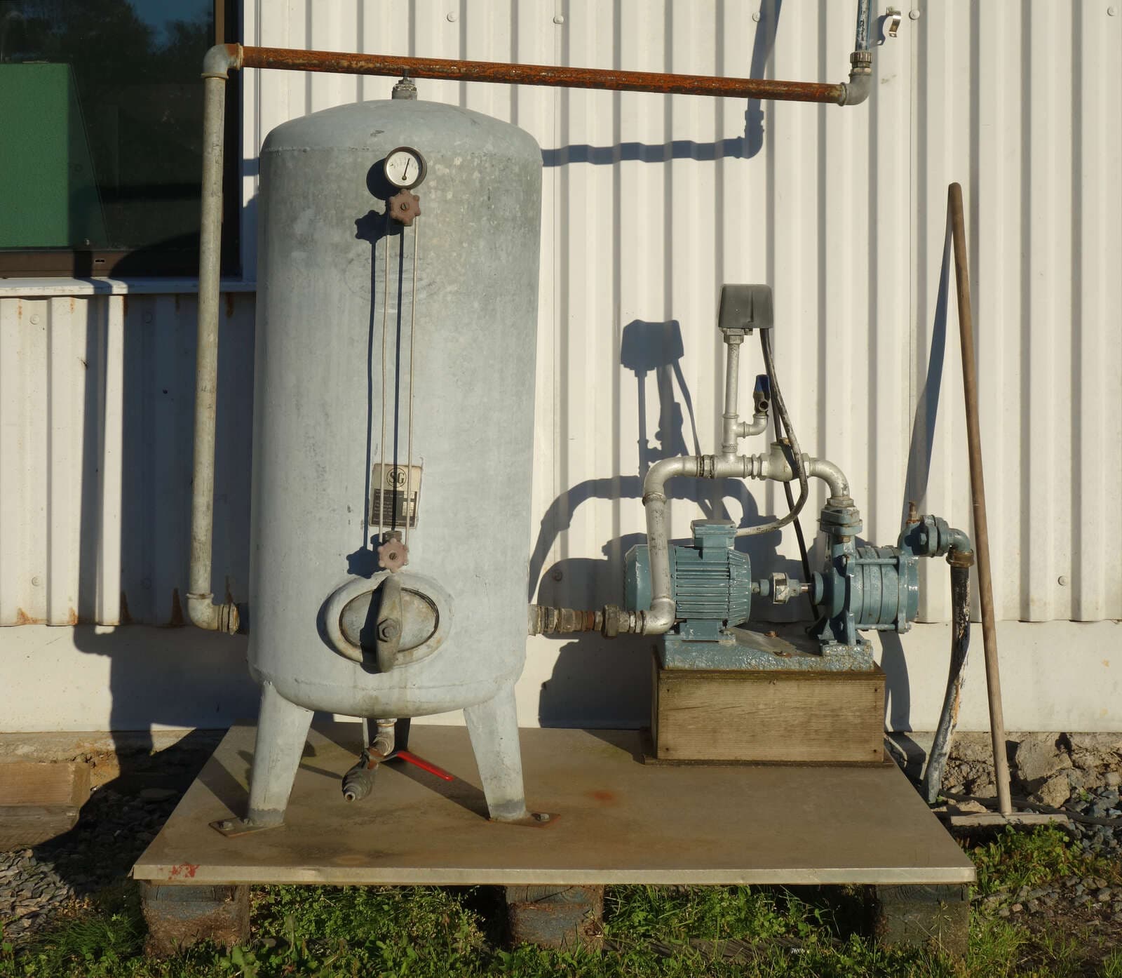 A well pressure tank and pump on a pad outside a building