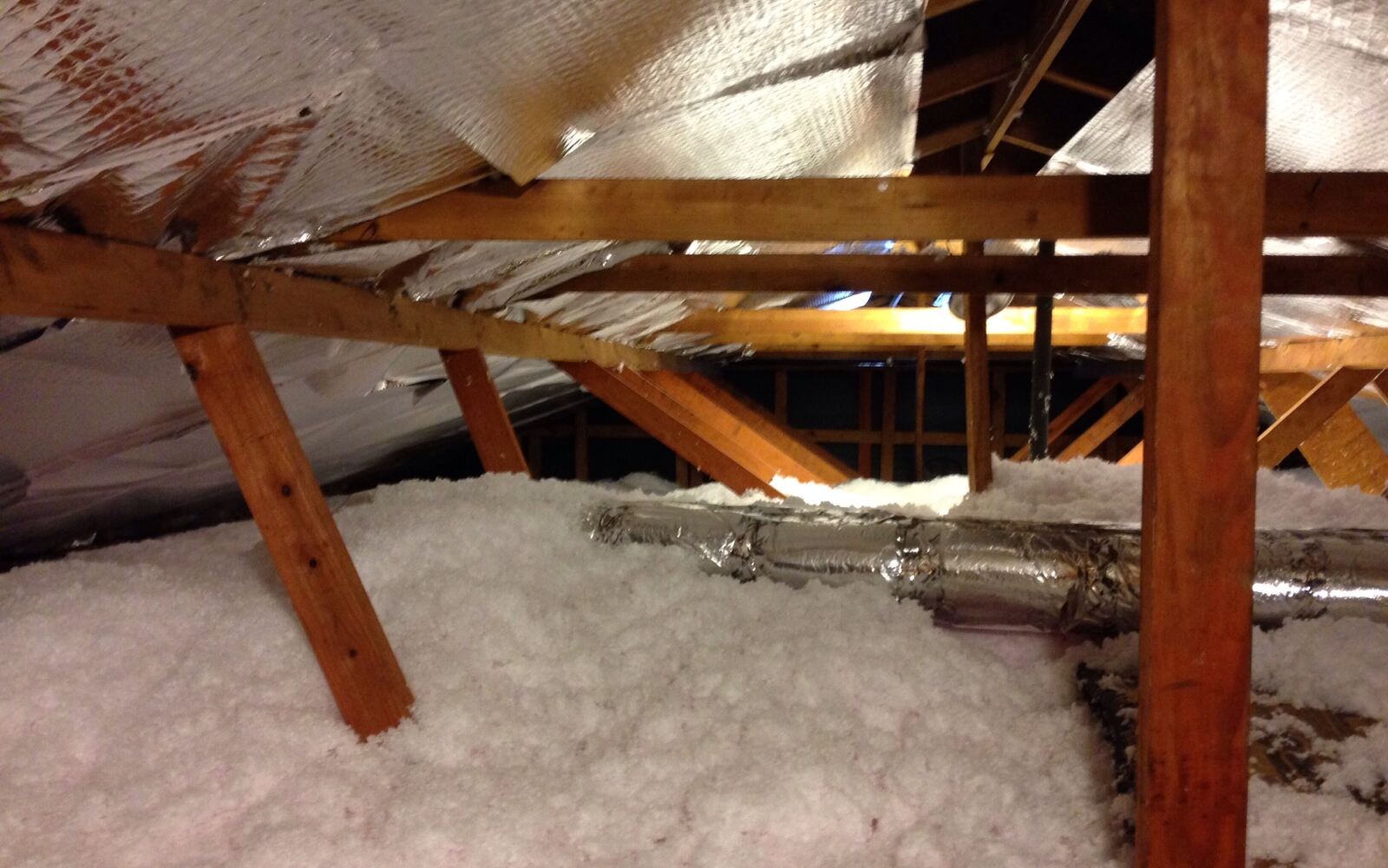 Blown-in attic insulation between rafters with a foil radiant barrier and insulated ducts
