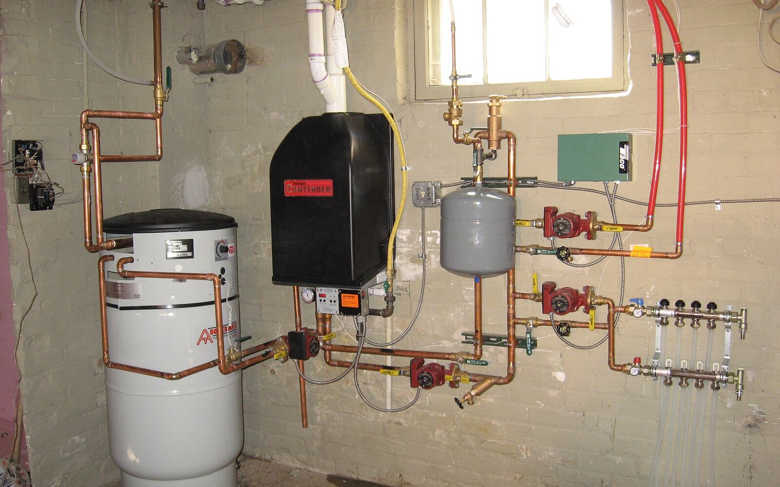 A basement mechanical room with a condensing boiler, indirect water heater, and copper piping