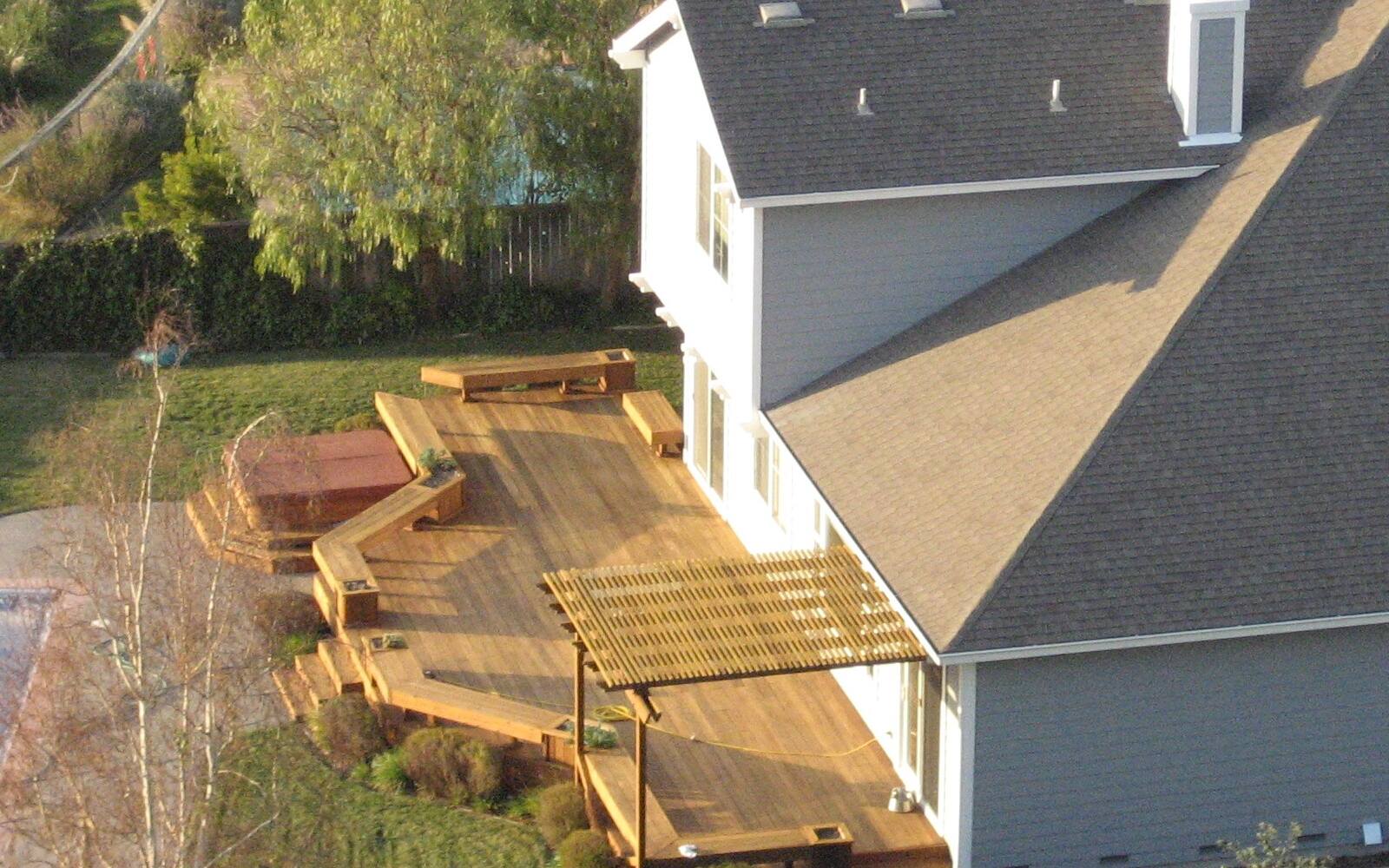 A multi-level wood deck with a pergola in a suburban backyard, seen from above